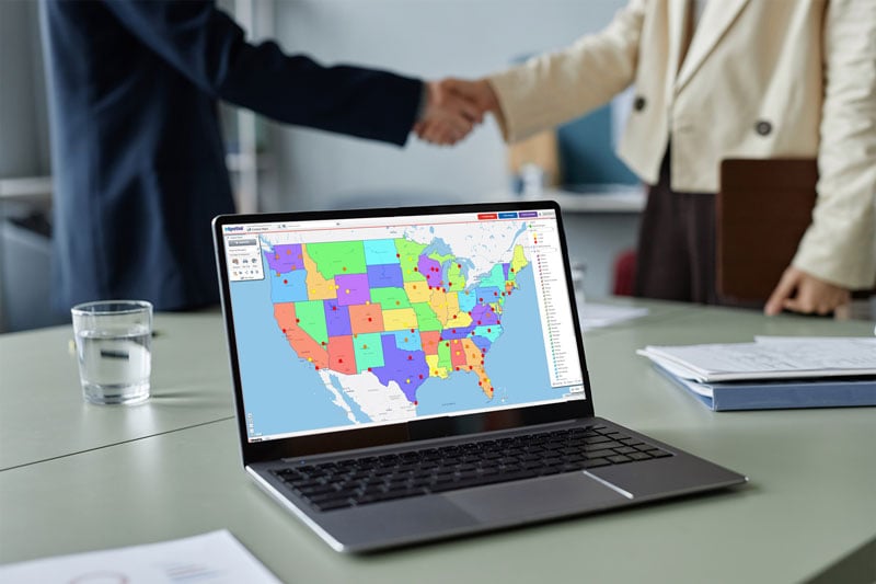 Map on a laptop screen, people shaking hands in background
